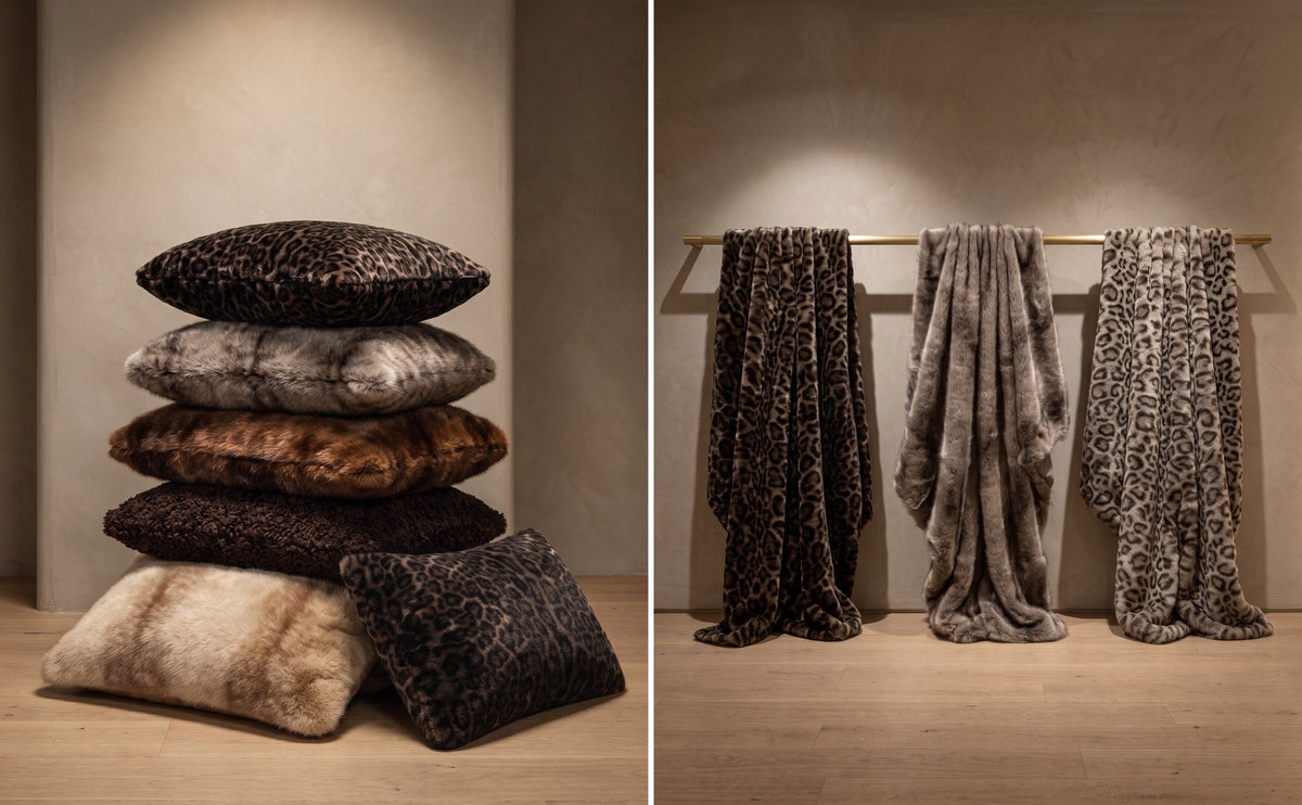 Coussins et plaids Apparis en fausse fourrure : coussins empilés en léopard, vison gris, vison, bouclette brown et vison blond, et trois plaids léopard foncé, vison gris et léopard clair suspendus à une barre dorée