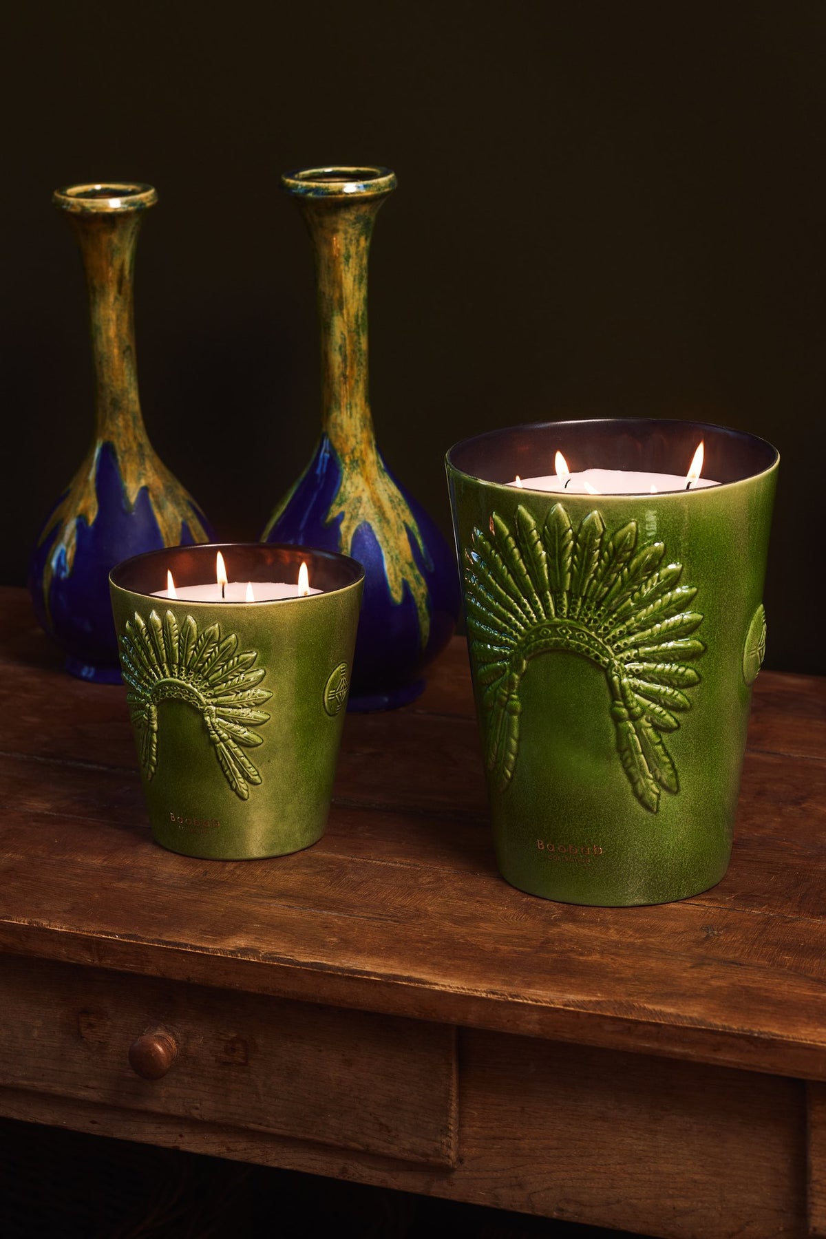 Deux bougies Baobab Sitting Bull allumées sur une table en bois, près de vases anciens