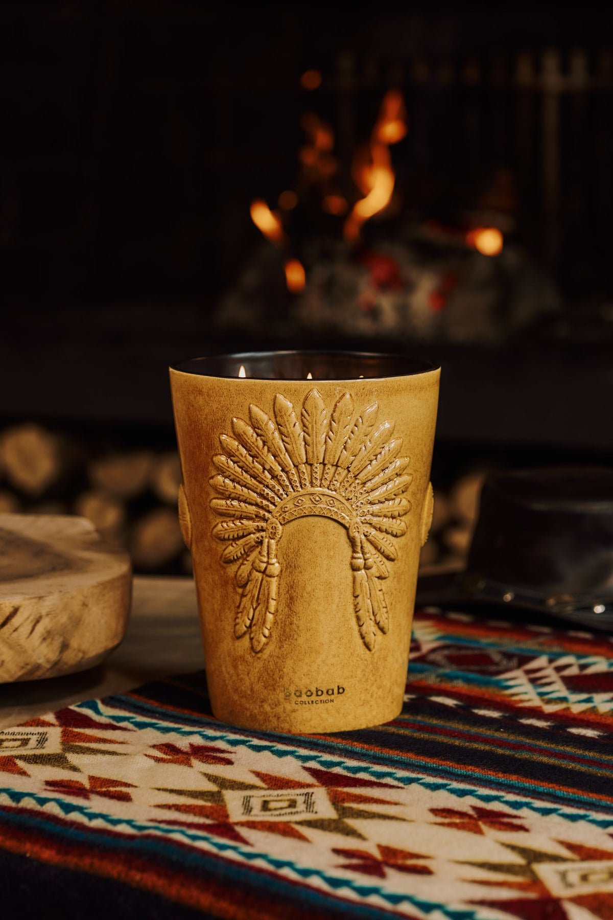 Bougie Baobab Geronimo posée sur un tissu à motifs, devant un feu de bois