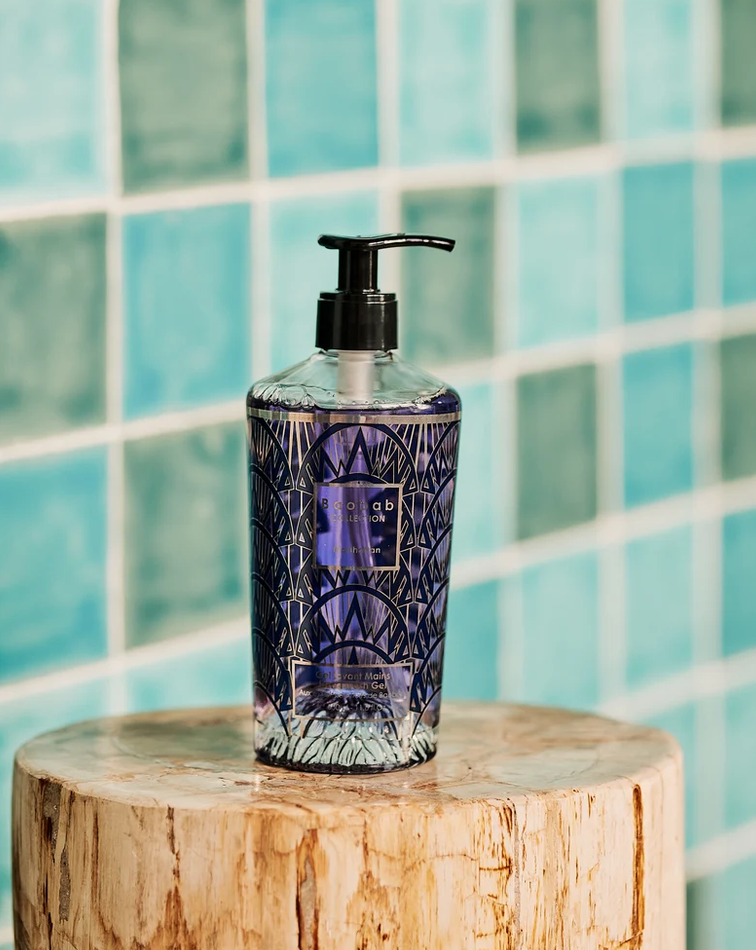 Gel lavant pour les mains Baobab Collection Manhattan posé sur un tabouret en bois devant un carrelage bleu